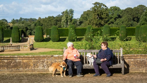 Visitors with their dogs sat on a bench on the North terrace at Montacute House